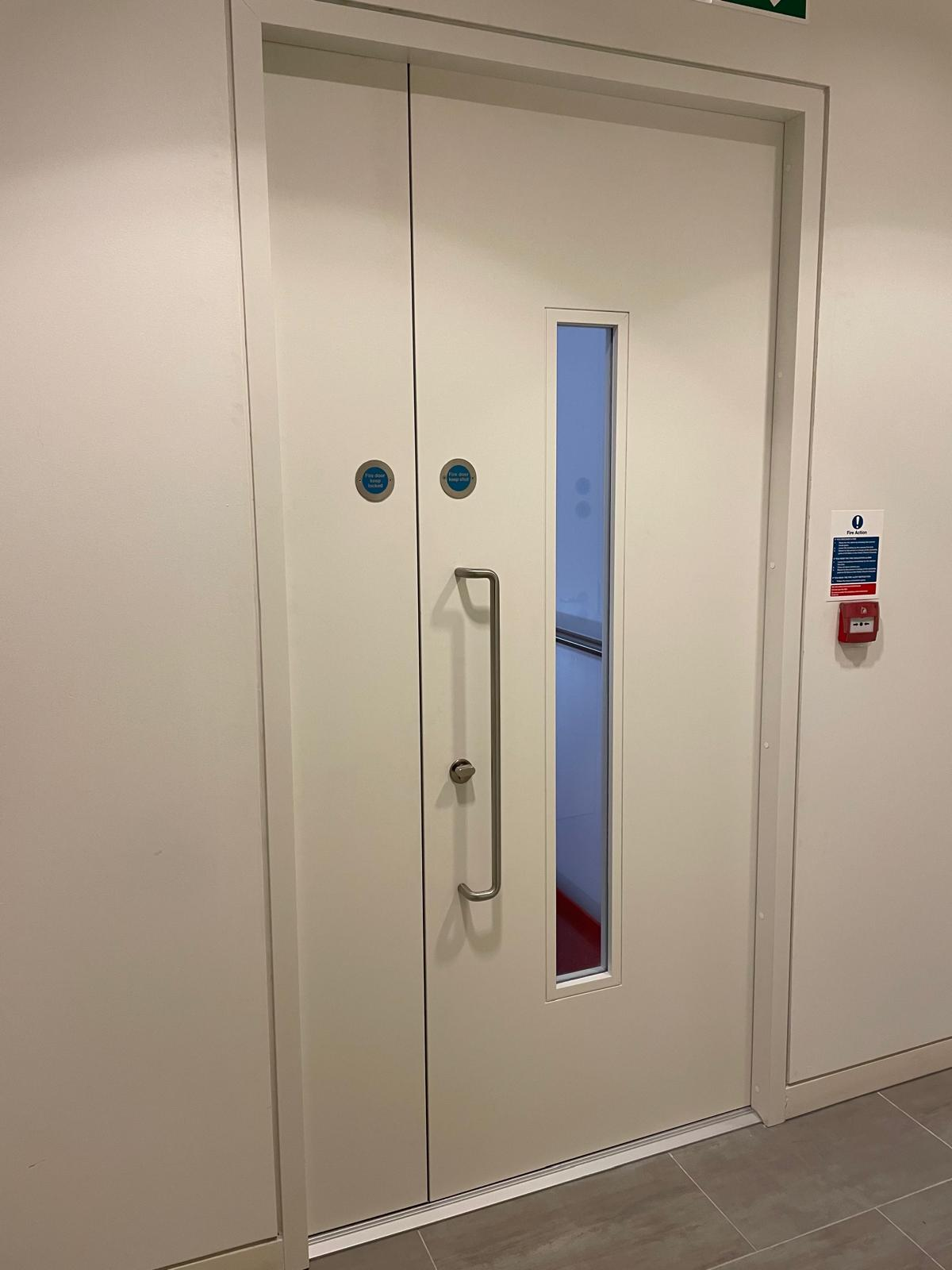 White double fire doors with a glazed vision panel and pull handle